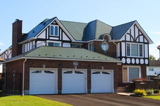 Tudor-style brick home with complex multi-hip Interlock aluminum shingle roof in Hunter Green, triple garage, dormers, and chimney in Nepean, ON.