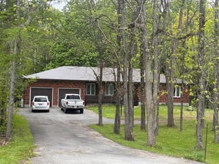 Single-storey brick ranch home in Richmond ON with Colonial Brown Interlock aluminum shingle roof, hip profile, viewed through mature trees from front-left.