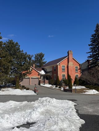 Two-storey red brick colonial home in Stittsville ON with Interlock Tile Red aluminum slate metal roof and prominent chimney, photographed in winter.