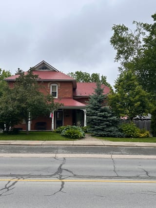 Two-storey Victorian brick home in Almonte, ON with a complex steep Tile Red Interlock aluminum shingle roof featuring a front dormer and wrap-around porch.