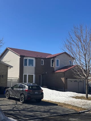 Two-storey brick suburban home in Orleans ON with Interlock Tile Red aluminum shingle metal roofing on a multi-hip complex roof, clear winter sky.