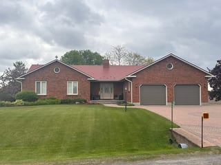 Front elevation of a brick ranch home with Interlock Tile Red aluminum shingle metal roof, dual gable peaks, chimney, and double garage in North Gower, ON.
