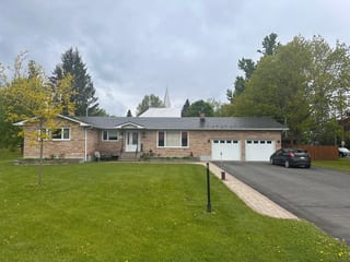 Front elevation of a single-storey ranch-style brick home in North Gower, ON, featuring a low-pitch black Interlock aluminum slate metal roof with chimney.
