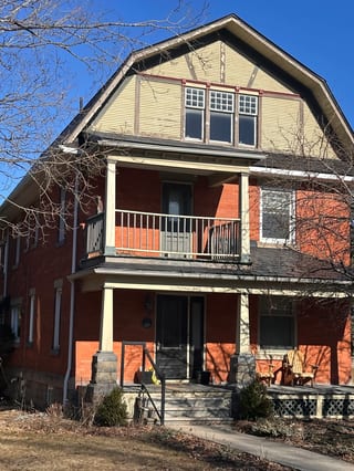 Black Interlock Slate aluminum roof on a red two-storey Craftsman home with dormers among tall, Kemptville, Ontario
