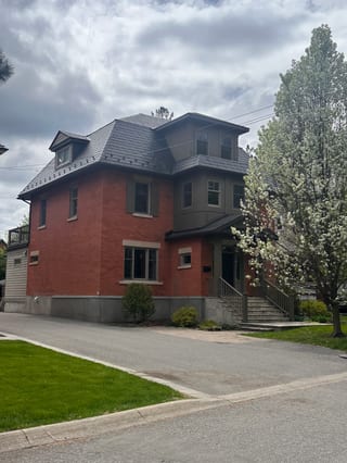 Heritage red-brick home in Ottawa with a dark charcoal Interlock aluminum slate mansard roof featuring dormers, viewed from the front-left.