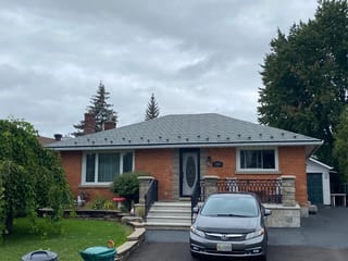 Hunter Green Interlock Slate aluminum roof on a red brick home with a grey metal roof among trees, Ottawa, Ontario