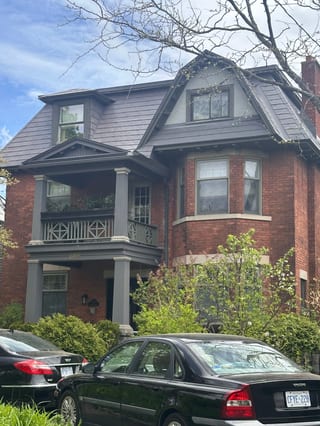 Three-storey Victorian red-brick home in Ottawa with Interlock Musket Grey aluminum slate roofing, multiple dormers, and a covered balcony entry.