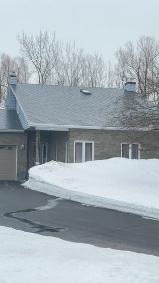 Black Interlock Slate aluminum roof on a grey brick home with a grey metal roof in the woods, Navan, Ontario