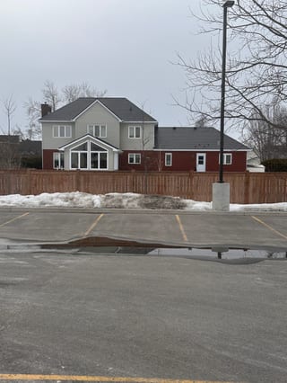 Rear elevation of a two-storey suburban home in Navan, ON with dark slate-profile Interlock aluminum roofing, red brick lower level, and gabled sunroom addition.