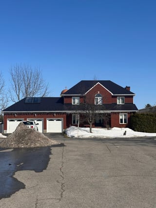 Two-storey red brick Colonial home in Navan ON with black Interlock aluminum slate roofing, turret, skylights, and triple-car garage in winter.