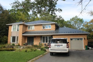 Deep Charcoal Interlock Slate aluminum roof on a tan brick two-storey home with dormers among tall pines, Kingston, Ontario