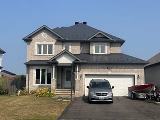Two-storey stone suburban home with Interlock deep charcoal aluminum slate metal roof, double garage, and multi-hip roofline in Russell, ON.