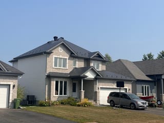 Two-storey suburban home in Russell, ON with Interlock deep charcoal aluminum slate metal roofing on a complex multi-hip roof with dormers and stone facade.