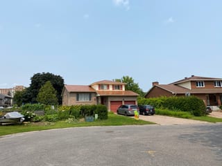 Street view of a two-storey brick home in Gloucester, ON with an Interlock Copper Penny aluminum slate metal roof and red garage doors.