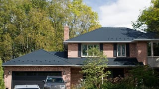 Two-storey brick Colonial home in Kingston, ON featuring a complex black Interlock aluminum slate metal roof with snow guards and brick chimney.