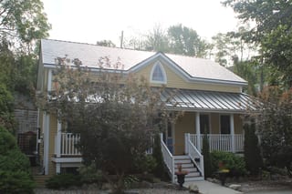 Black Interlock Slate aluminum roof on a yellow single-storey cottage among tall trees, Kingston, Ontario