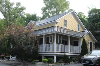 Black Interlock Slate aluminum roof on a yellow two-storey home with dormers among tall pines, Kingston, Ontario