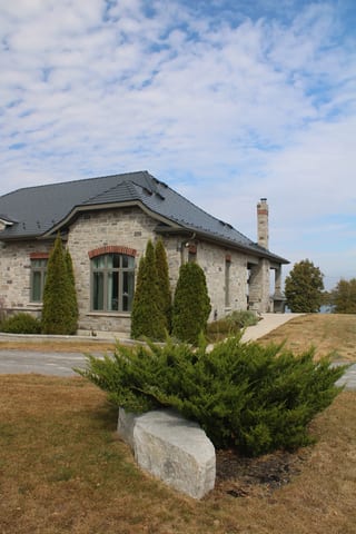 Deep Charcoal Interlock Slate aluminum roof on a Deep Charcoal metal roof on a stone Craftsman-style home, Picton, Ontario