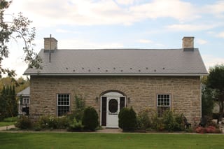 Deep Charcoal Interlock Slate aluminum roof on a tan stone cottage with a metal roof among green trees, Carleton Place, Ontario