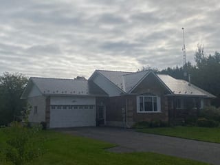 Ranch-style brick home in Winchester ON featuring Interlock Tudor Brown aluminum slate metal roofing with multi-gable complex roof profile under overcast skies.