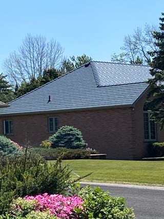 Single-storey brick Colonial home in Cornwall, ON with a hip-style Interlock aluminum slate roof in Deep Charcoal, surrounded by mature trees and manicured landscaping.