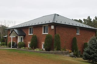 Black Interlock Slate aluminum roof on a red brick home with a metal roof and bushes in a rural, Carrying Place, Ontario