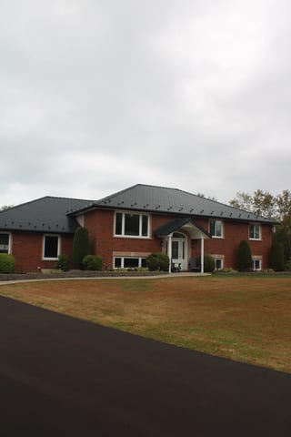 Black Interlock Slate aluminum roof on a red brick home with white trim and a black metal roof in, Carrying Place, Ontario