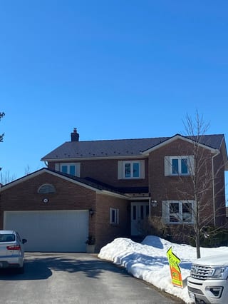 Two-storey brick Colonial home in Belleville ON with Interlock Tudor Brown aluminum slate metal roof, chimney, and snow guards on a clear winter day.