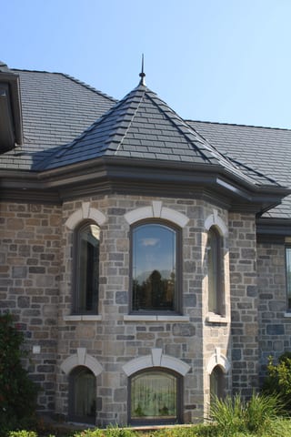 Deep Charcoal Interlock Slate aluminum roof on a grey stone home with dormers set among tall trees, Alexandria, Ontario