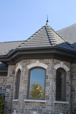 Deep Charcoal Interlock Slate aluminum roof on a grey Colonial home with a stone facade and arched windows, Alexandria, Ontario