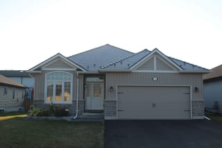 Tudor Brown Interlock Slate aluminum roof on a brown single-storey home with a metal roof among tall, Belleville, Ontario