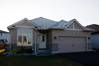 Single-family ranch-style home in Belleville ON with Interlock Tudor Brown aluminum slate metal roofing featuring multi-hip complex roof profile and stone accent base.
