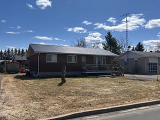 Front elevation of a 1-storey brick ranch home in Chesterville, ON, featuring a low-pitch Interlock black aluminum slate metal roof with light snow dusting.