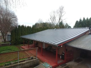 Deep Charcoal Interlock Standing Seam aluminum roof on a red single-family home with a metal roof in a forested, Scio, Oregon