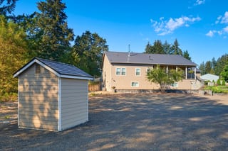 Rear elevation of a ranch-style home in Lebanon, OR featuring Interlock black aluminum slate metal roofing with a medium-pitch gable profile and detached storage shed.