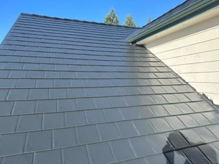 Close view of a black Interlock aluminum slate metal roof on a single-family home in Eugene OR, showing crisp panel alignment and hip geometry.