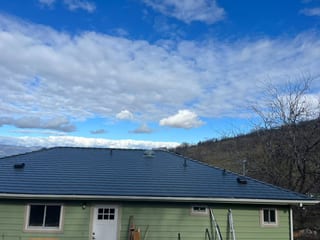 Deep charcoal Interlock aluminum slate metal roof on a single-story ranch-style home with green siding, set against a hillside in The Dalles, OR.