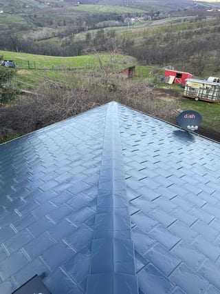 Ridge-line view of a deep charcoal Interlock aluminum slate roof on a rural farmhouse in The Dalles, OR, with rolling green hills behind.