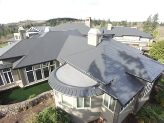Deep Charcoal Interlock IB Membrane aluminum roof on a beige single-family home with a metal roof in a forested, Turner, Oregon