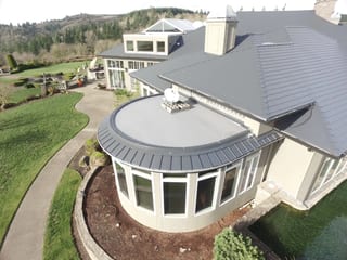 Deep Charcoal Interlock IB Membrane aluminum roof on a beige home with a metal roof among forested hills, Turner, Oregon