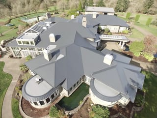 Deep Charcoal Interlock IB Membrane aluminum roof on a white house with a grey metal roof in a forested area, Turner, Oregon