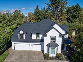 Deep Charcoal Interlock Shake aluminum roof on a white two-storey home with dormers among tall evergreen, Portland, Oregon