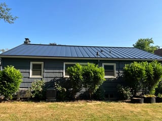 Black Interlock Standing Seam aluminum roof on a dark home with a metal roof among greenery in a, Portland, Oregon