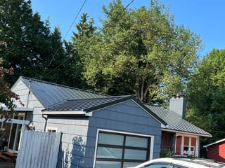 Black Interlock Standing Seam aluminum roof on a grey home with a metal roof among tall trees, Portland, Oregon