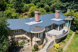 Deep Charcoal Interlock Slate aluminum roof on a tan two-storey Colonial home with a balcony among tall, Portland, Oregon
