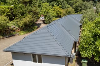 Deep Charcoal Interlock Slate aluminum roof on a white single-family home with a metal roof among trees, Portland, Oregon