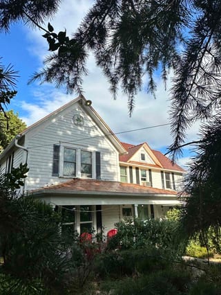 Two-story Victorian home in McMinnville, OR with Interlock Copper Penny cedar-shingle aluminum metal roofing, steep gabled dormers, and a wrap-around porch.