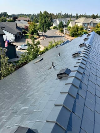 Aerial view of Interlock aluminum slate metal roofing in charcoal-black on a two-story craftsman home in Oregon City, OR, showing ridge vents and vent pipes.