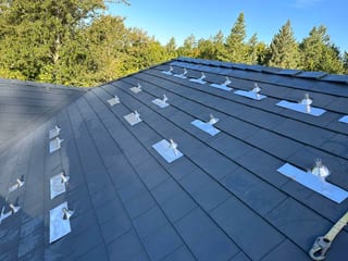 Deep charcoal Interlock aluminum slate metal roof on a hip-style home, featuring numerous silver vent pipe flashings across the field in Portland, OR.