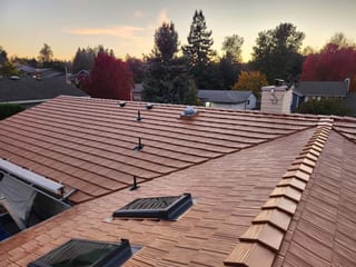 Aerial view of a complex Interlock aluminum shake roof in Copper Penny on a suburban Ranch home in Salem OR, featuring valleys, skylights, and ridge caps at golden hour.